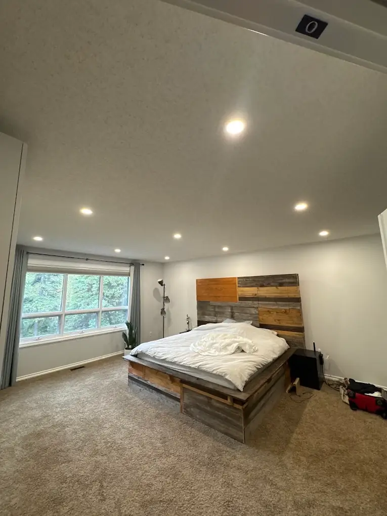 Bedroom with a grid of recessed pot lights above a reclaimed wood headboard