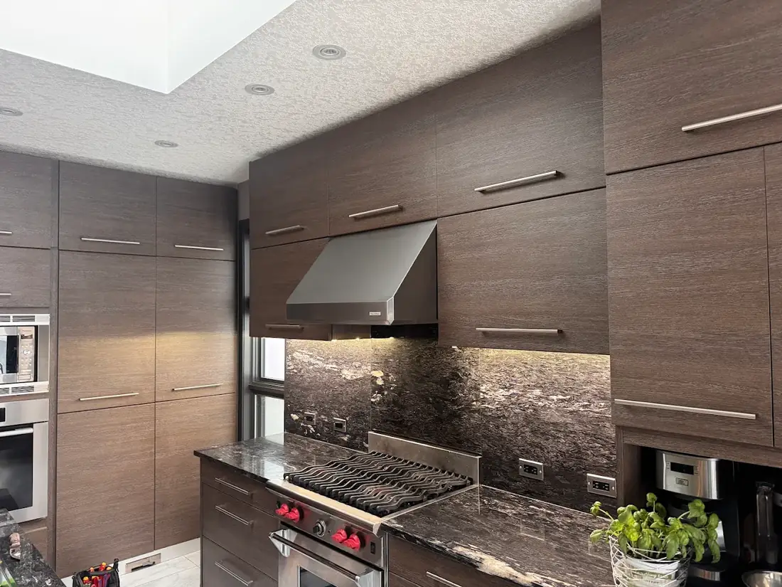 Dark wood kitchen with recessed pot lights and a lit granite backsplash